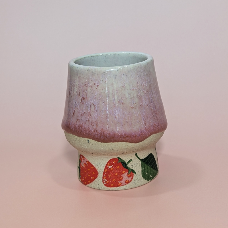A cup with flowing pink glaze that tapers at the mouth.