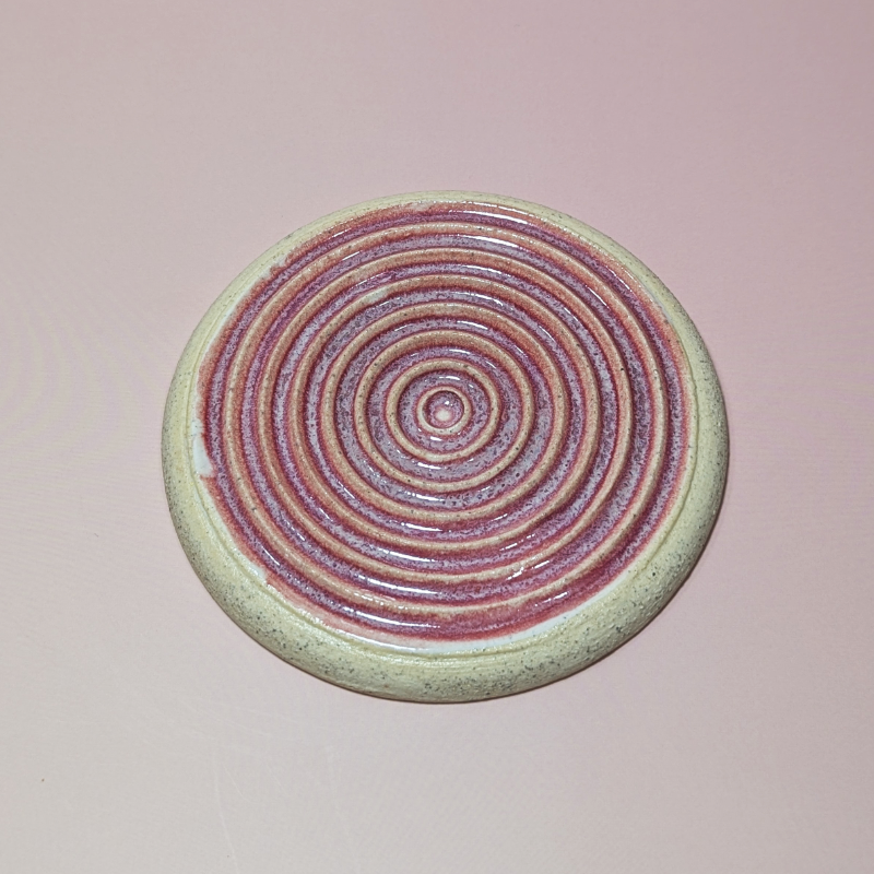 The image shows a dark pink glaze settling into the ridges of the grater.
