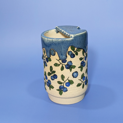 3 quarter view showing the back of the sippy cup. The scalloped edge design of the lid is visible.