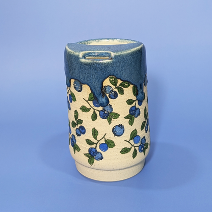Front facing view of a sippy cup. It features flowing blue glaze and blueberry and leaf design.
