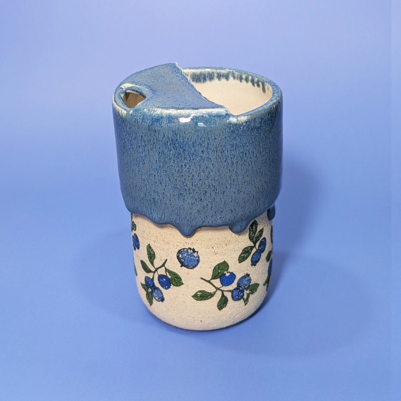 This sippy cup has flowing blue glaze that covers the top half and a pattern of blueberry and leaves all the way around the base.